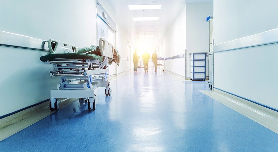Corridor of a hospital, an empty patient stretcher and three surgeons in the distance