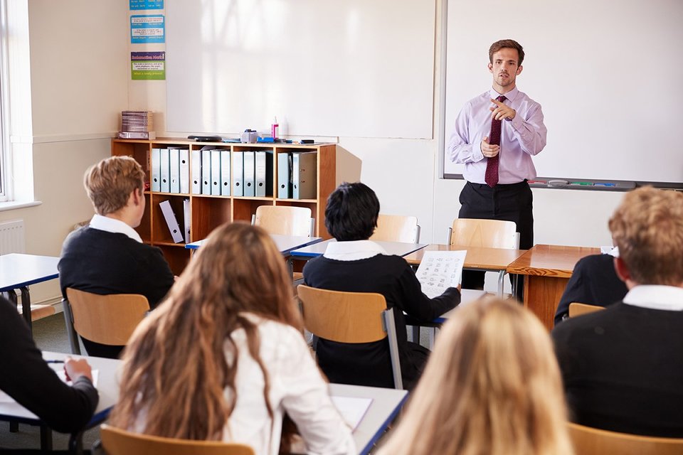 male teacher standing a school classroom full of students 