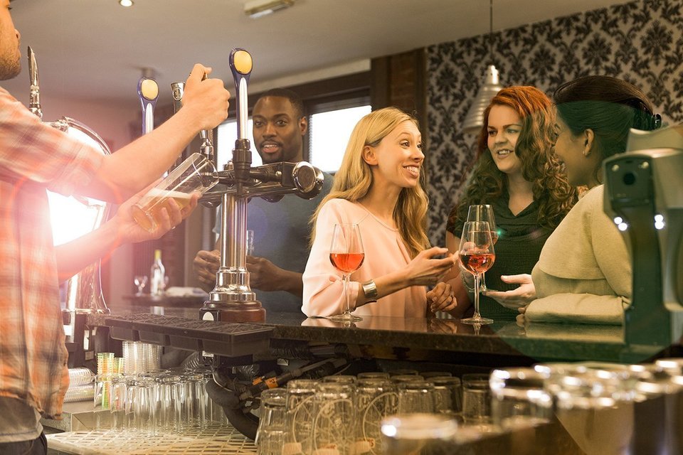 Members of the public enjoying drinks at the bar area of a busy pub 