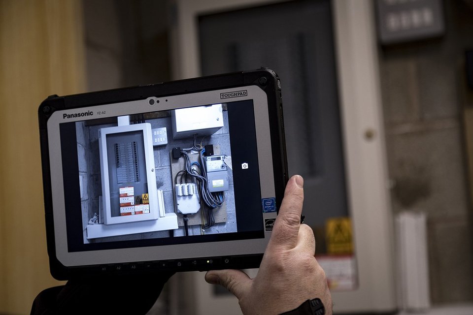 Engineer holding up a Panasonic rugged tablet to take an image of circuit board